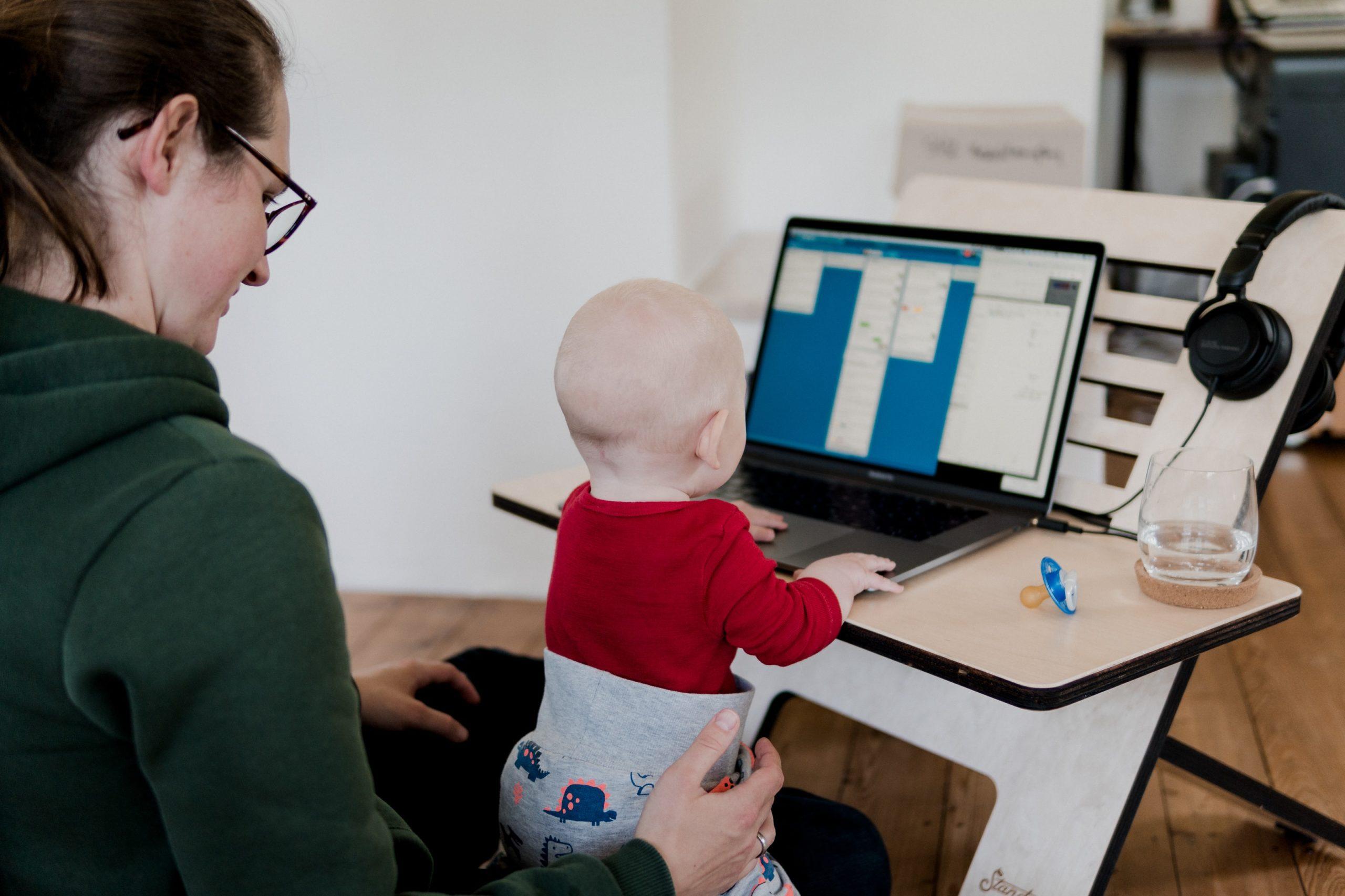 Frau sitzt mit Baby auf dem Schoß vorm Laptop