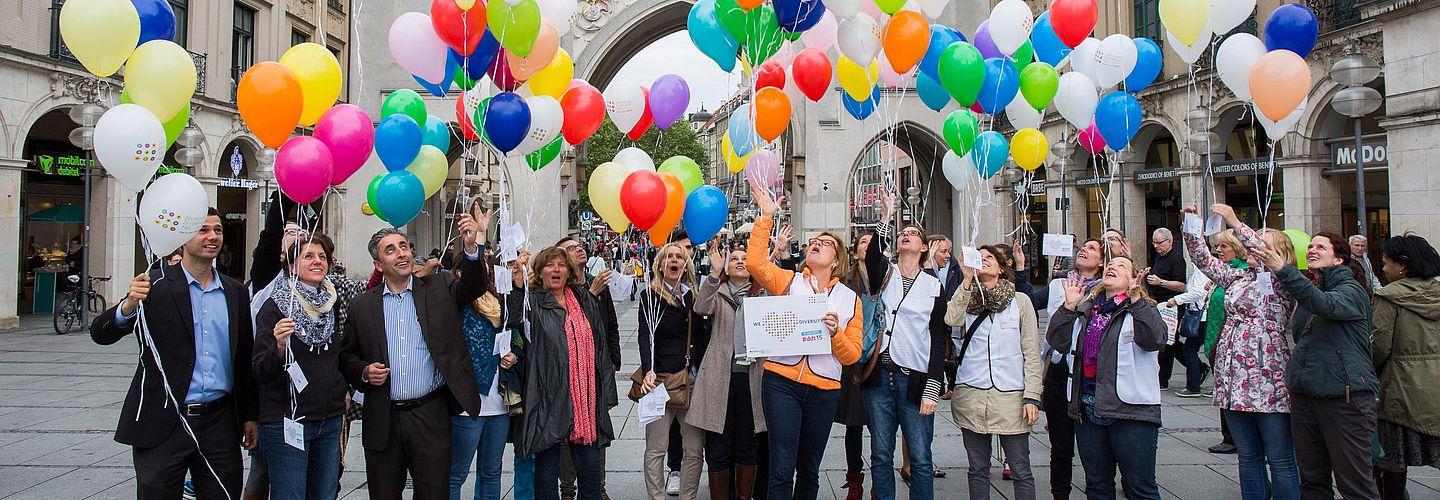 Eine Gruppe von Menschen lässt bunte Luftballons steigen.